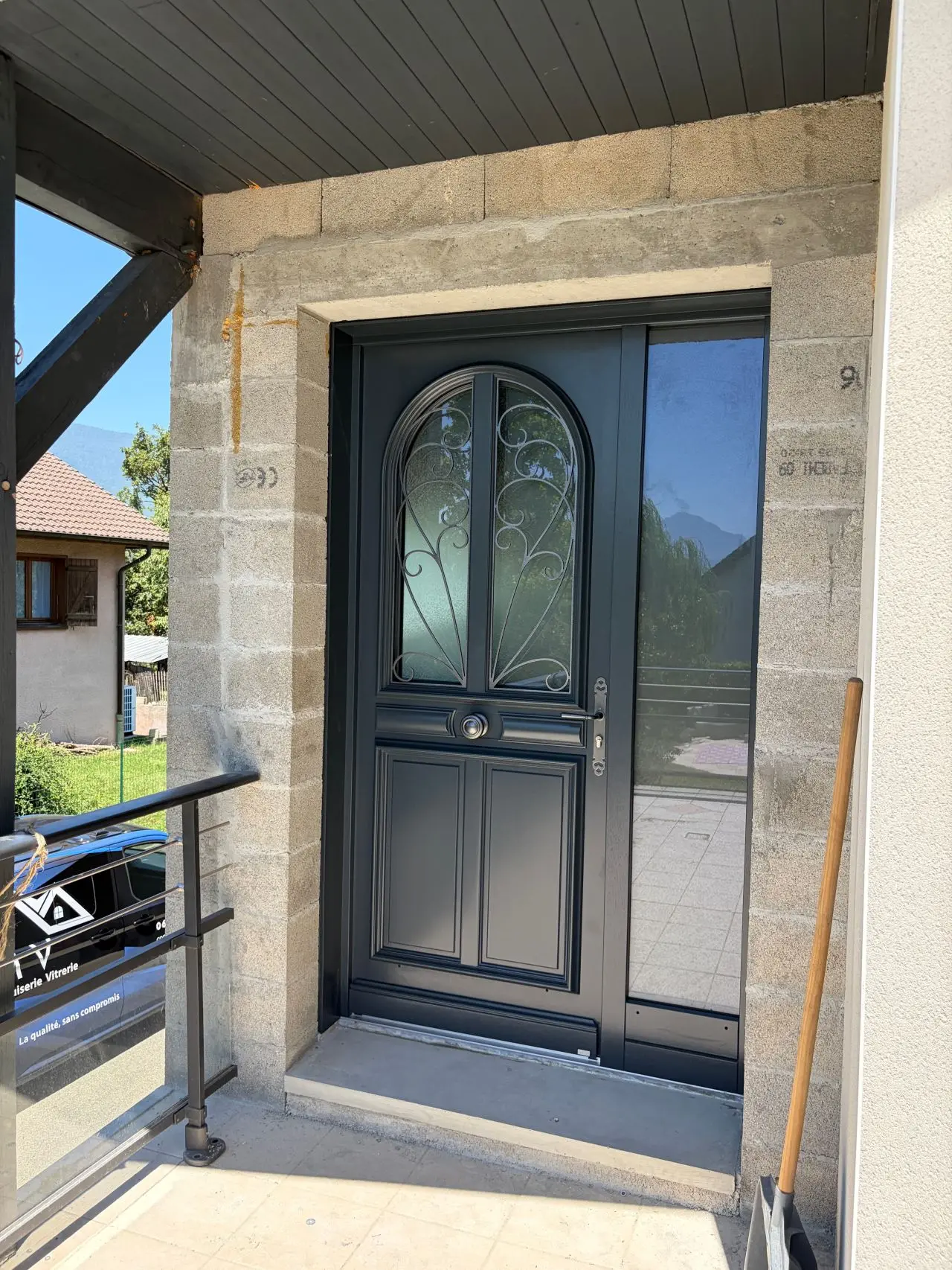 Porte d’entrée noire cintrée avec vitrage, dans un encadrement de pierre de taille.