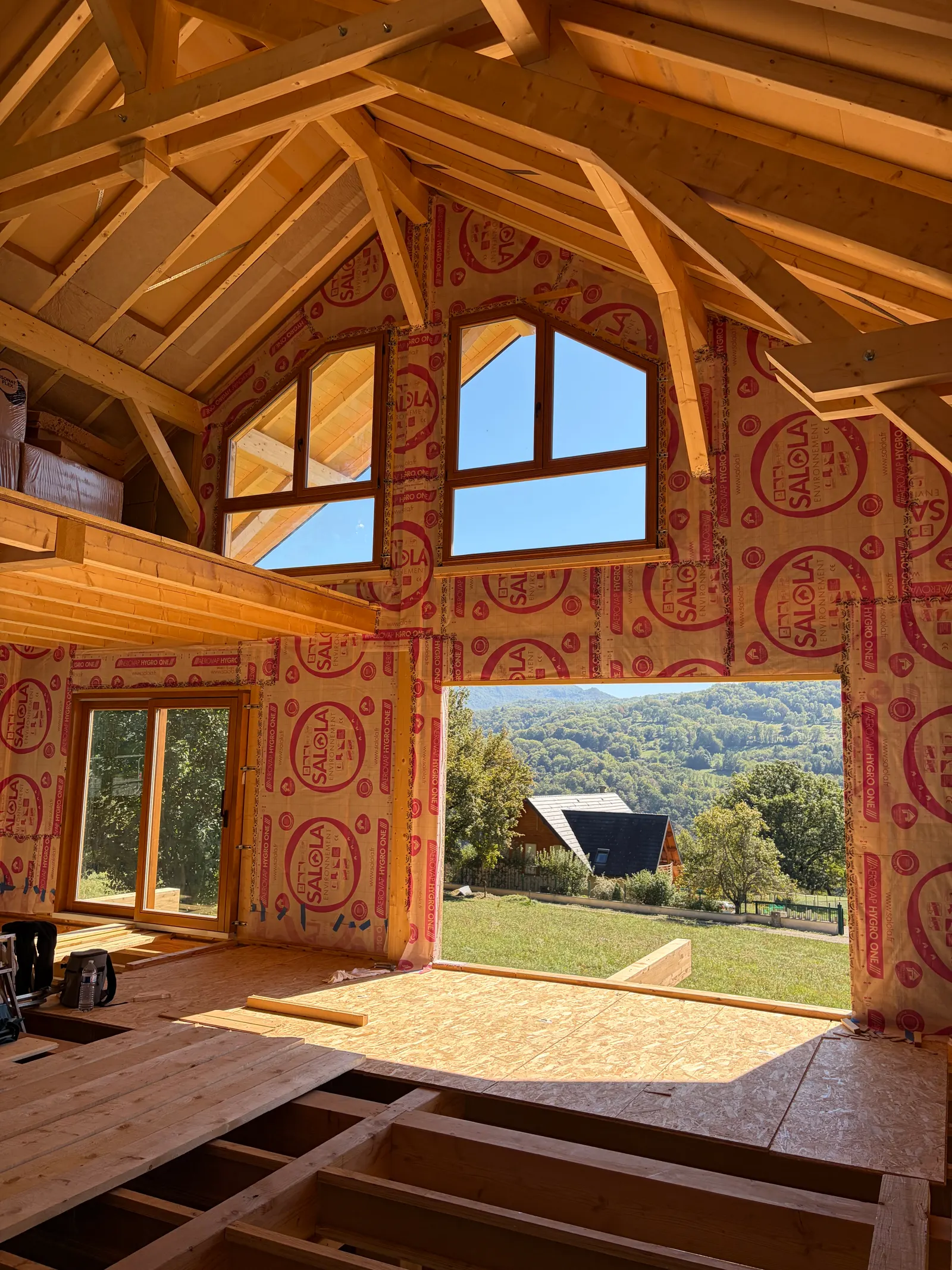 Chalet à ossature bois en cours de pose : fenêtres cintrées sous la charpente, ouvertes sur la vallée.