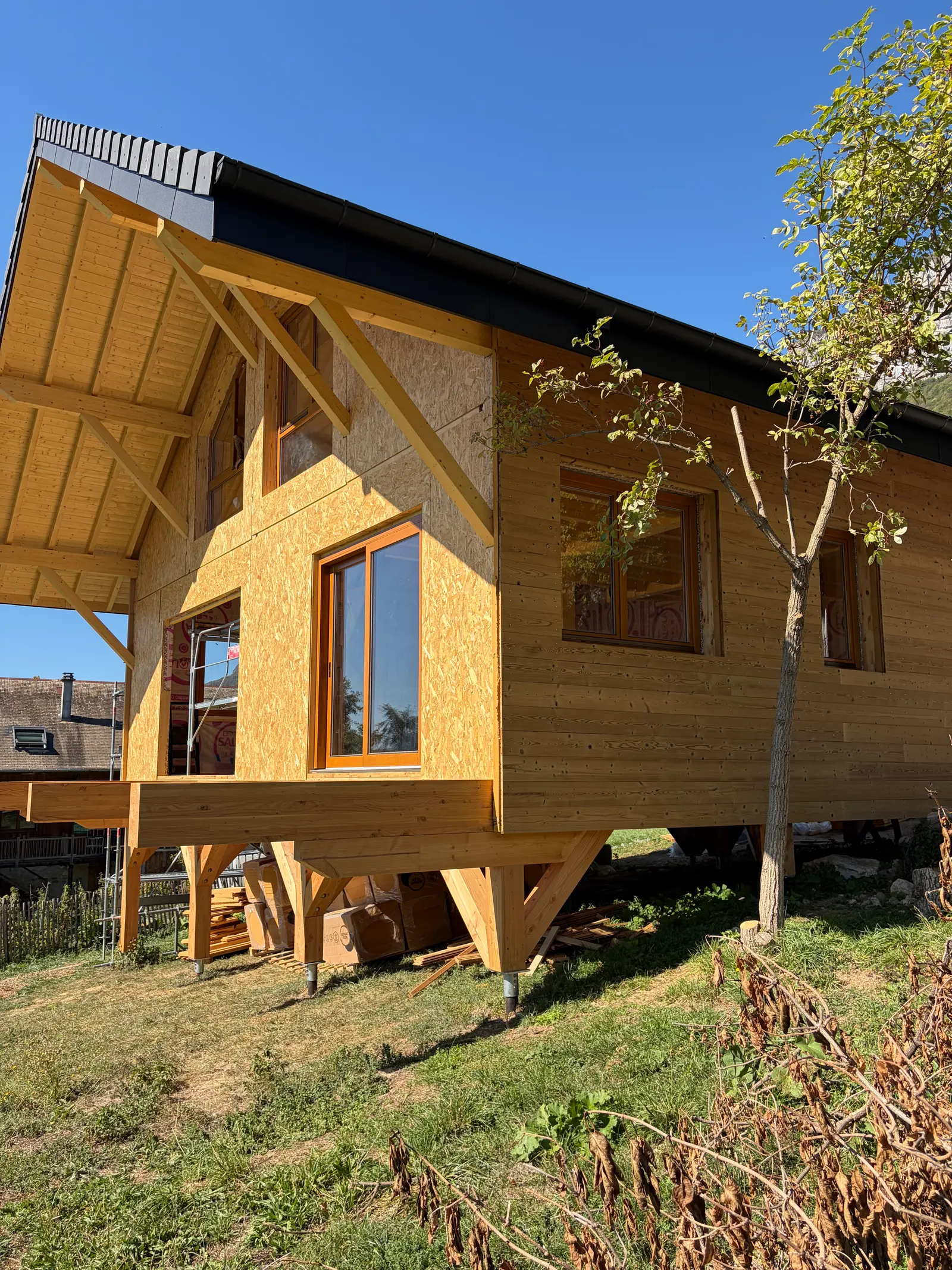 Le chalet vu de l’extérieur, sur pilotis, avec ses menuiseries bois posées.