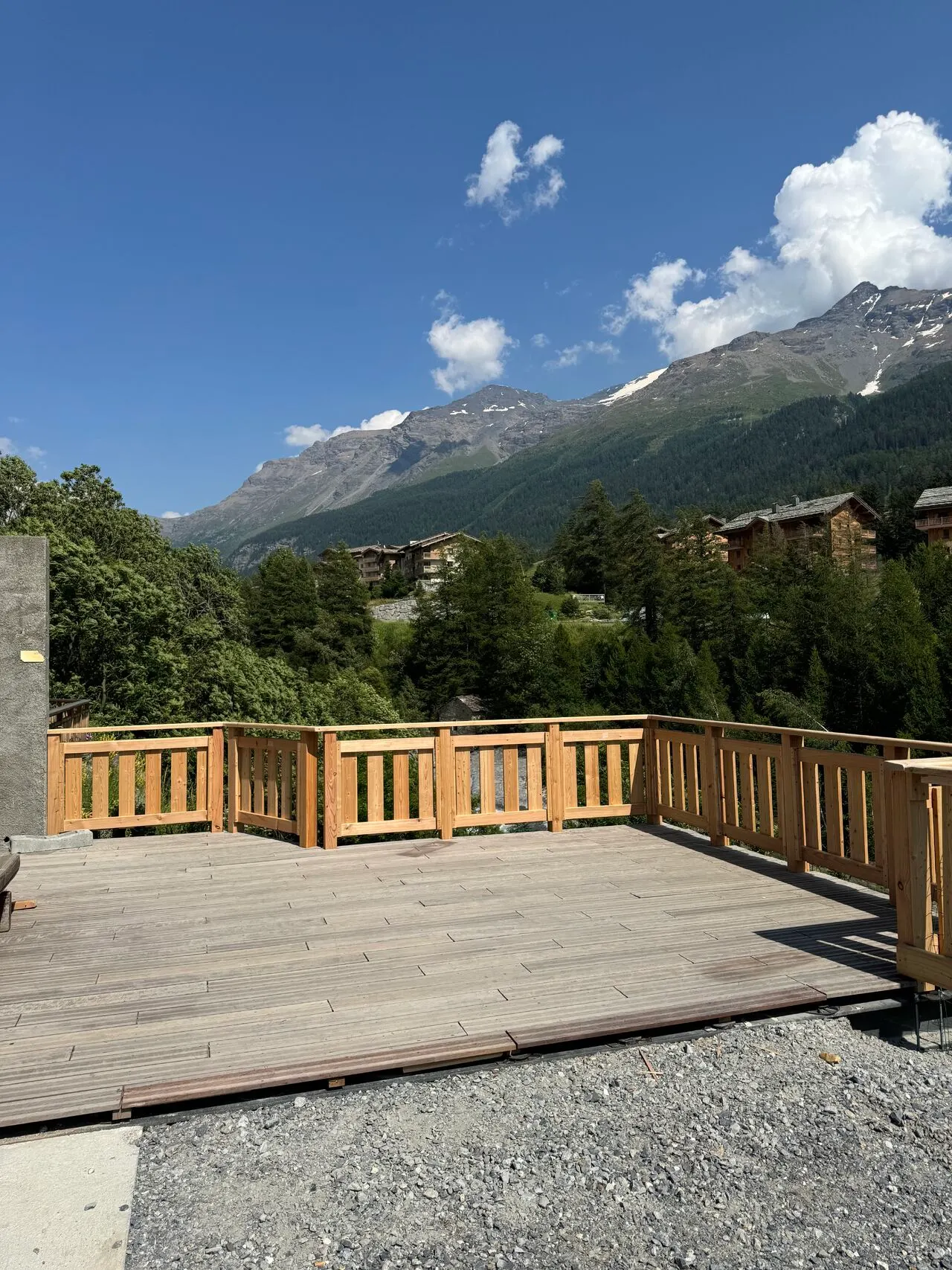 Terrasse en bois bordée d’un garde-corps en bois, face aux montagnes.