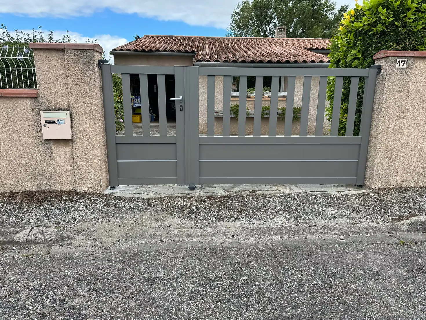 Portail ajouré gris sur un muret enduit, en bord de rue.
