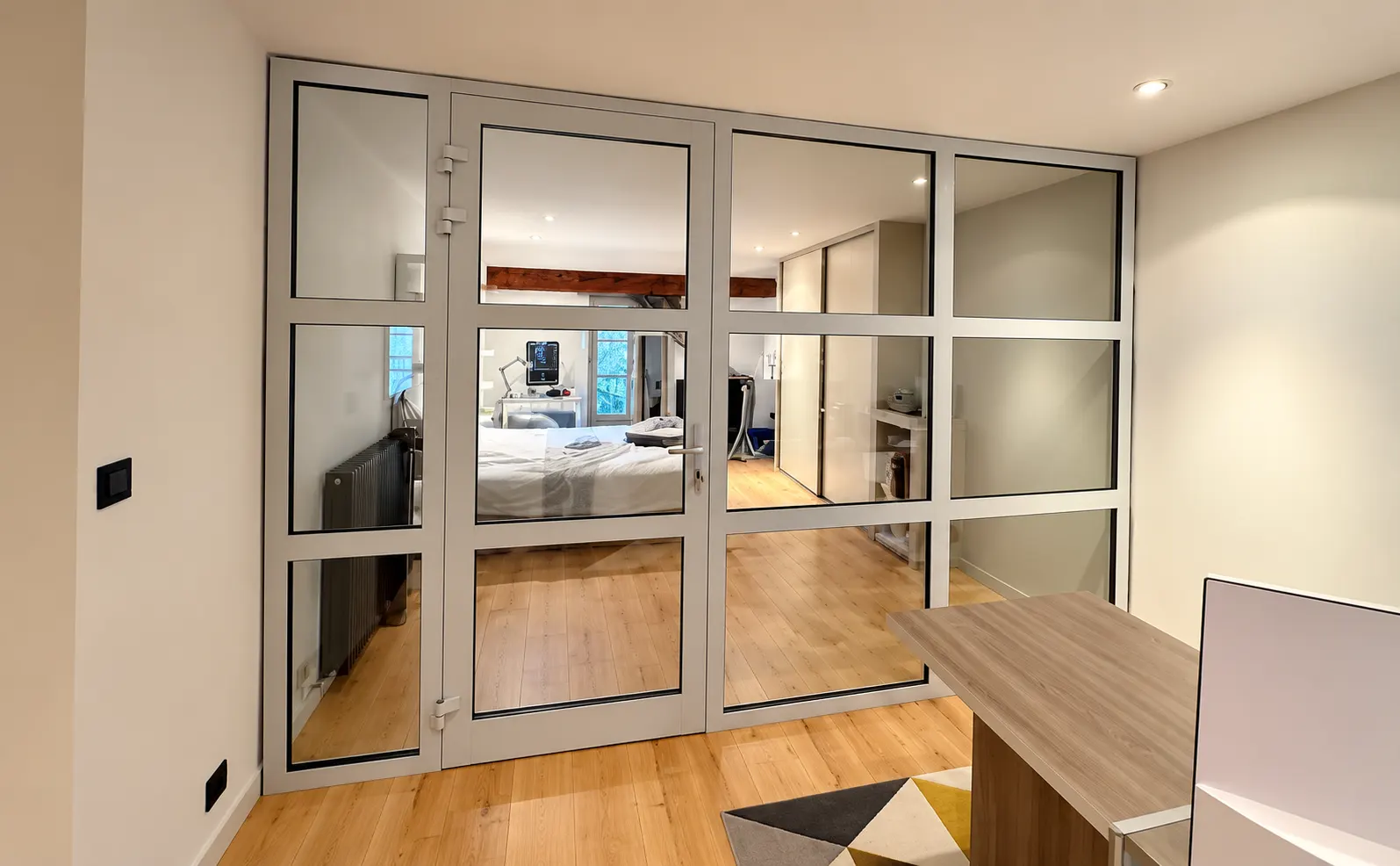 Cloison vitrée claire à portes, séparant un bureau d’une chambre.